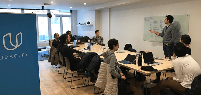 Udacity learners in a workshop session with an instructor at a whiteboard.